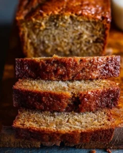 A loaf of moist banana bread sliced on a wooden cutting board