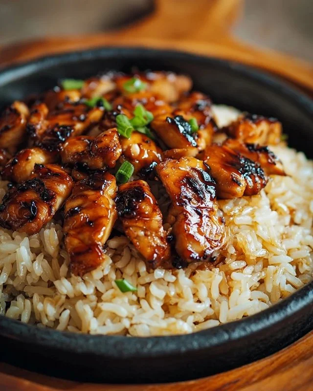 Plate of honey BBQ chicken served over a bed of rice with fresh herbs.