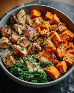 A colorful bowl of healthy chicken and sweet potatoes garnished with vegetables.