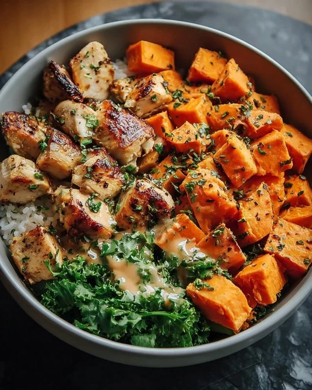 A colorful bowl of healthy chicken and sweet potatoes garnished with vegetables.